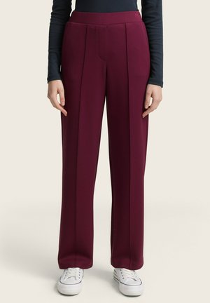 Pantalons plissés bordeaux à taille haute et jambes larges. Fabriqués en tissu texturé, associés à des baskets blanches et un haut sombre.
