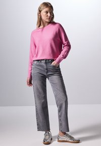 Pull en tricot rose avec un col rond, associé à un jean droit gris clair. Baskets métalliques argentées avec des semelles marron et une finition texturée.