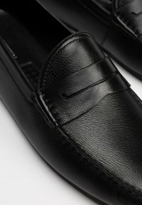 Mocasines de cuero negro con acabado texturizado, que presentan una banda de acento cosida y una puntera lisa. Diseño elegante adecuado para uso formal o informal.