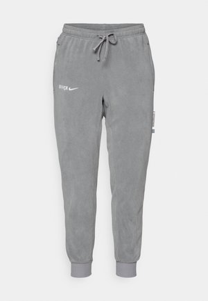 Calças de treino cinzentas feitas de felpa macia, com uma cintura elástica, cordão e punhos canelados. Inclui os logótipos "BARÇA" e "Nike".