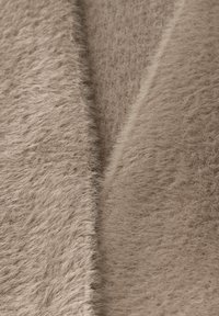 Tissu beige duveteux, présentant une texture douce avec une finition légèrement brillante. La surface montre une apparence uniforme et moelleuse.