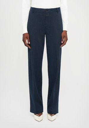 Navy blue wide-leg trousers made of smooth fabric, featuring a front button closure and side pockets, paired with pointed white heels.