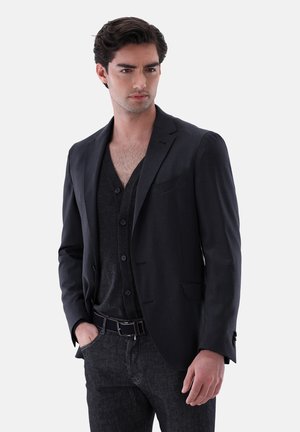 Dark grey blazer with sharp lapels, single button closure, and subtle pocket. Worn over a black v-neck shirt, paired with dark denim jeans.