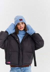 Čierna prešívaná bunda s krátkym strihom, vybavená zipsom a dvoma prednými vreckami. Kombinovaná so svetlomodrou chlpatou čiapkou a svetrom.