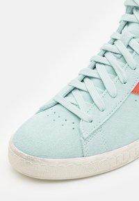 Baskets en suede bleu clair avec lacets, trous de ventilation sur l'orteil, détail en stripe rouge et semelle en caoutchouc blanc texturé.