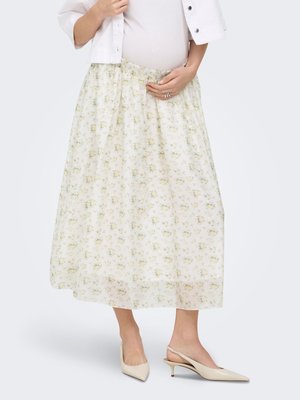Mujer embarazada sujetándose la barriga, con una falda midi blanca con flores, camiseta blanca, chaqueta sobre el hombro y zapatos slingback crema de tacón bajo.