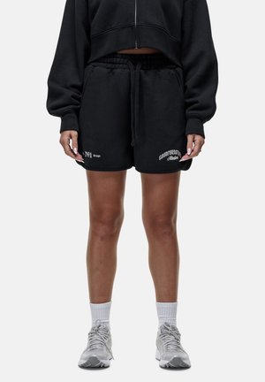 Zwarte shorts van katoen, met een elastische tailleband en trekkoord. Versierd met witte geborduurde tekst op de onderkant vooraan.