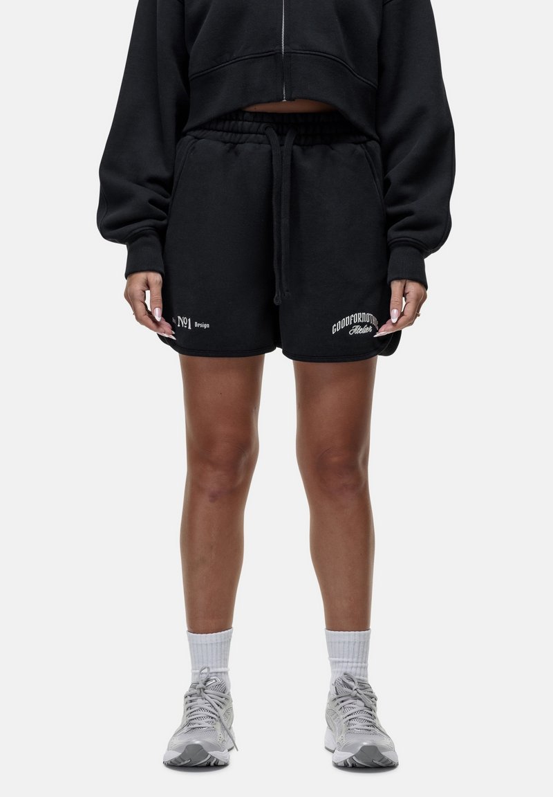 Pantaloni corti neri in cotone, con vita elasticizzata e cordoncino. Decorati con testo ricamato bianco nella parte bassa anteriore.