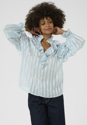 Light blue blouse with ruffled collar and cuffs, featuring a striped pattern and small white dots. Soft, sheer fabric.