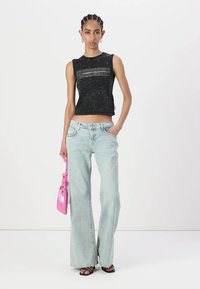 Svart ärmlös topp med texturerat mönster och framgående randdetalj, matchad med ljustvättade vida jeans och en liten rosa handväska.