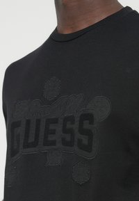 Μαύρο βαμβακερό T-shirt με ανυψωμένα μαύρα λογότυπα και λεπτομέρειες. Σχεδίαση με λαιμόκοψη, υφασμένα μοτίβα και κεντήματα.