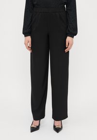 Pantalons larges noirs en tissu lisse avec une taille élastique, présentant une coupe décontractée et un léger éclat.