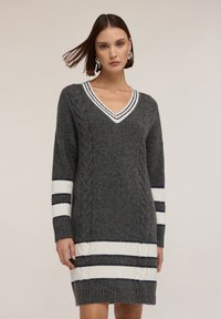 Abito grigio a maglia con scollo a V, texture a trecce e dettagli a righe bianche e navy sulle maniche e sull'orlo. Maniche lunghe, lunghezza sopra il ginocchio.