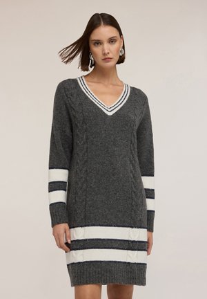 Szara dzianinowa sukienka z dekoltem w serek, teksturą splotu warkoczowego oraz białymi i granatowymi pasami na rękawach i u dołu. Długie rękawy, długość lekko powyżej kolan.