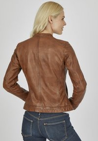 Braune Lederjacke mit tailliertem Design, das über Rippdetails an den Schultern und eine glatte Textur verfügt. Die Rückansicht zeigt die maßgeschneiderte Form.