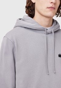 Grijze hoodie met een trekkoord en een gestructureerde stof. Bevat een klein zwart logo aan de voorkant. Soepele, casual uitstraling.