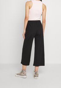 Pantalons larges noirs avec une taille élastique, associés à un débardeur rose clair à côtes et des baskets montantes à motifs.
