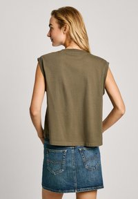 Alyvuogių žaliai be rankovių marškinėliai, pagaminti iš medvilnės, su apvaliu iškirpimu ir laisvu siluetu, derinami su džinsiniu mini sijonu, turinčiu galinius kišenius.