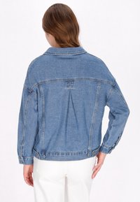 Jeansjacka i medelblått med en plissé bak, knappdetaljer vid ärmsluten och en avslappnad passform. Har en klassisk krage.