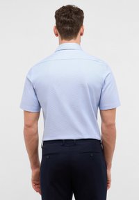 Lichtblauwe short-sleeve shirt met subtiele ruitpatroon, standaard kraag en achterste yoke-detail, gecombineerd met donkere broek met knoopaccenten.