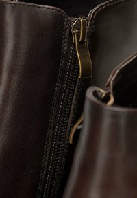 Botas tobilleras de cuero marrón con cremallera lateral, que presentan un tirador de cremallera en tono dorado y costuras en contraste a lo largo de las costuras.