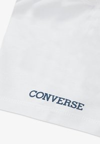 Hvit bomullsstoff med en glatt tekstur, med en marineblå "CONVERSE"-logo trykt nederst. Enkelt design uten ytterligere mønstre.
