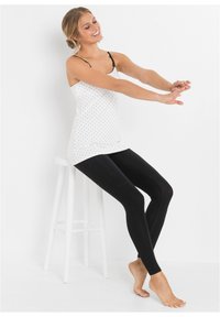 Camisola bianca con pois neri e spalline sottili, abbinata a leggings neri uni. Entrambi i tessuti sembrano lisci e aderenti.