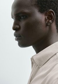 Profilo di una persona che indossa una camicia colletto beige chiaro. La pelle è scura con una texture liscia e presenta un'acconciatura a taglio corto.