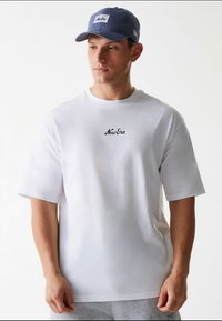 Vit t-shirt med korta ärmar och rund halsringning, med subtil svart "New Era"-broderi. Bärs med en blå basebollkeps.