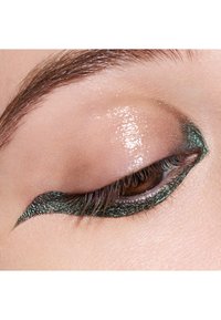 Green glitter eyeliner applied in a sharp winged design on a closed eyelid, with glossy skin and defined lashes.