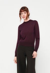 Langärmliger Pullover mit Rundhalsausschnitt in tiefem Lila, aus weichem, feinem Strickmaterial, kombiniert mit weiten schwarzen Hosen. Schlichtes, tailliertes Design.