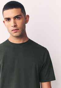 Tumehe rohelise värvusega puuvillane T-särk lühikeste varrukatega ja ümmarguse kaelusega. Materjal tundub sile ja kerge ning kortse on vähe.