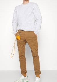 Sweat-shirt gris, chinos couleur sable et baskets blanches avec des accents verts. Accessoire jaune avec une sangle suspendu au pantalon. Ourlets retroussés.