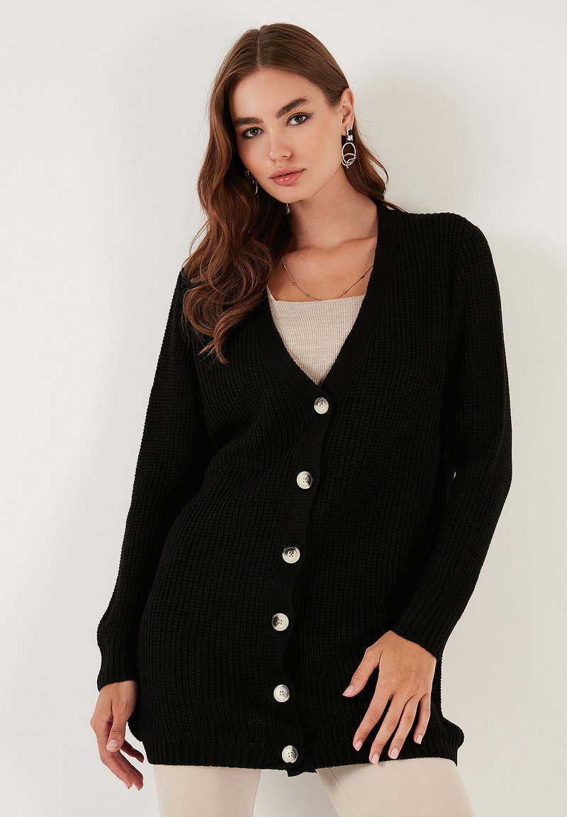 Fekete kötött kardigán V-nyakkal, hosszú ujjal és nagy ezüst színű gombokkal. Bordázott textúrájú és hosszú, laza fazonú.
