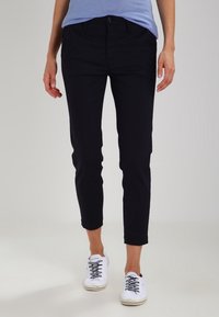 Svarta cropped byxor gjorda av lättviktig tyg med slim fit. I kombination med vita sneakers som har snörning och en texturerad yta.
