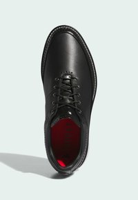 Czarne skórzane buty z zaokrąglonym noskiem, sznurowane, z perforowanymi detalami, czerwoną wkładką oznaczoną "BOOST" oraz białą podeszwą.