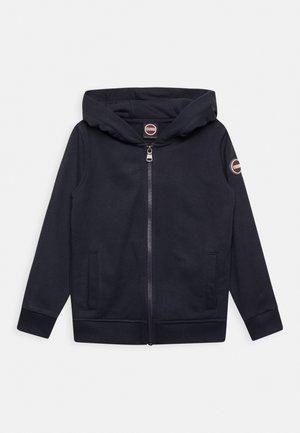 Sudadera con capucha azul marino con cremallera, bolsillos frontales, puños y bajo acanalados, parches con marca en el pecho y el brazo izquierdo, y capucha incorporada.