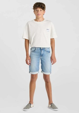 T-shirt en coton blanc, shorts en denim bleu clair avec des revers, et chaussures slip-on noir et blanc à carreaux. Design simple, coupe décontractée.
