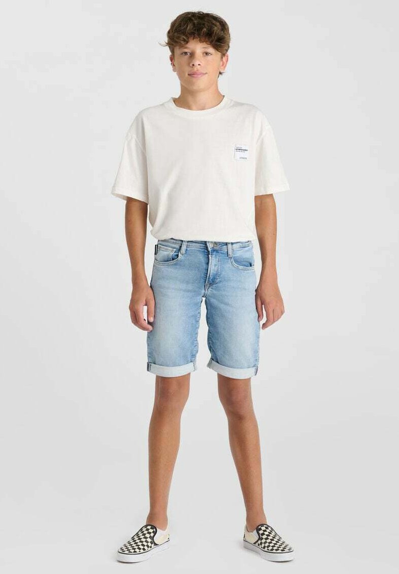 T-shirt en coton blanc, shorts en denim bleu clair avec des revers, et chaussures slip-on noir et blanc à carreaux. Design simple, coupe décontractée.