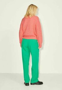 Pull rose tricoté avec une coupe ample et une texture côtelée, associé à un pantalon vert droit. Des bottines noires complètent la tenue.