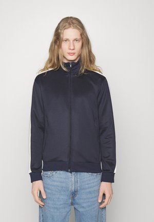 Marineblaues Zip-Jackett aus glattem Material, mit weißen Seitenstreifen, einem hohen Kragen und gerippten Bündchen und Saum.