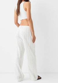 Vita, broderade, lätta, vida byxor med elastisk midja, med ett blommönster. Matchas med en åtsittande vit crop-top.