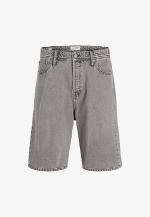 Dreng står og smiler iført en beige strikket kortærmet skjorte, grå knælange shorts, hvide sokker og sorte sko på en ensfarvet baggrund.