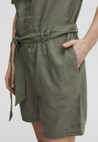 Olivengrüner Leinen-Overall mit einem taillierten Gürtel, kurzen Ärmeln und frontalen Taschen. Verfügt über einen strukturierten Stoff und eine Knopfleiste.