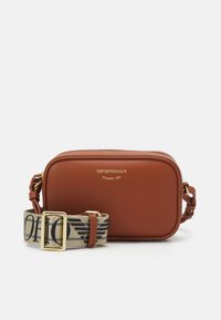 Brun skinn crossbody-veske med teksturert overflate, gullfarget metallbeslag og et mønstret stoffreim med fet skrift. Rektangulær form.