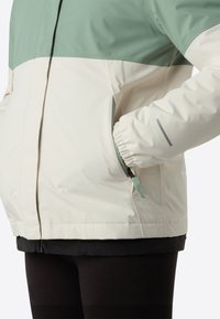 Veste légère avec un design bicolore, comprenant une partie supérieure vert menthe, une partie inférieure crème et des poignets élastiques. Comprend des poches latérales.