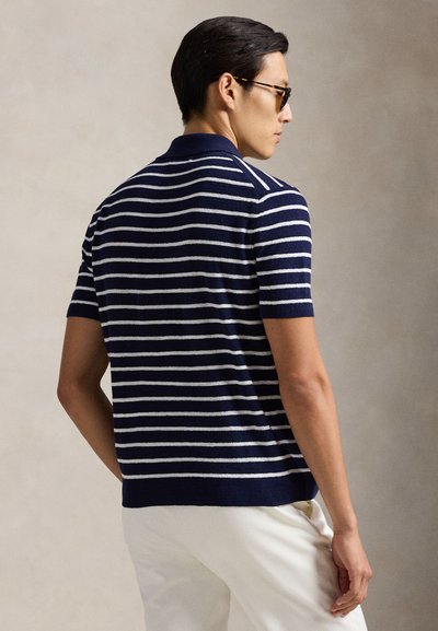 Tengerészkék rövid ujjú galléros póló fehér csíkokkal, klasszikus gallérral és bordázott szegéllyel, puha kötött anyagból készült.