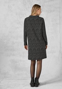 Musta-valkoinen herringbone-kuosiset mekko, jossa on pitkät hihat, polvimittainen ja korkeakauluksinen; yhdistettynä mustiin nilkkabootseihin.