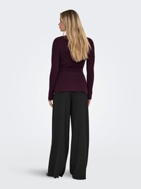 Dugi rukav, rebrasti džemper tamnoljubičaste boje, prilagođen u struku, s A-linijom i suptilnim bočnim otvorima, upareno s crnim hlačama širokih nogavica.