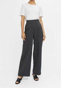 Pantalons larges en tissu à motifs gris foncé, taille haute, associés à un t-shirt blanc uni et des sandales noires à enfiler.